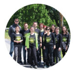 Gruppe von Menschen mit schwarzen T-Shirts und grünen Schriftzügen, die im Freien auf einem Weg vor Bäumen stehen