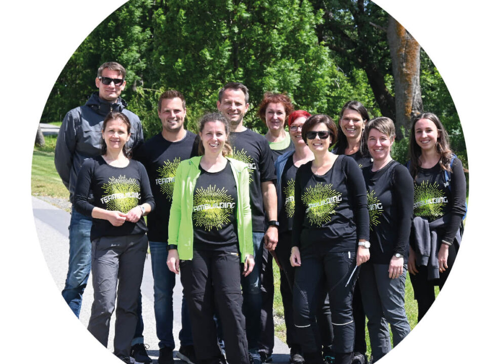 Gruppe von Menschen mit schwarzen T-Shirts und grünen Schriftzügen, die im Freien auf einem Weg vor Bäumen stehen